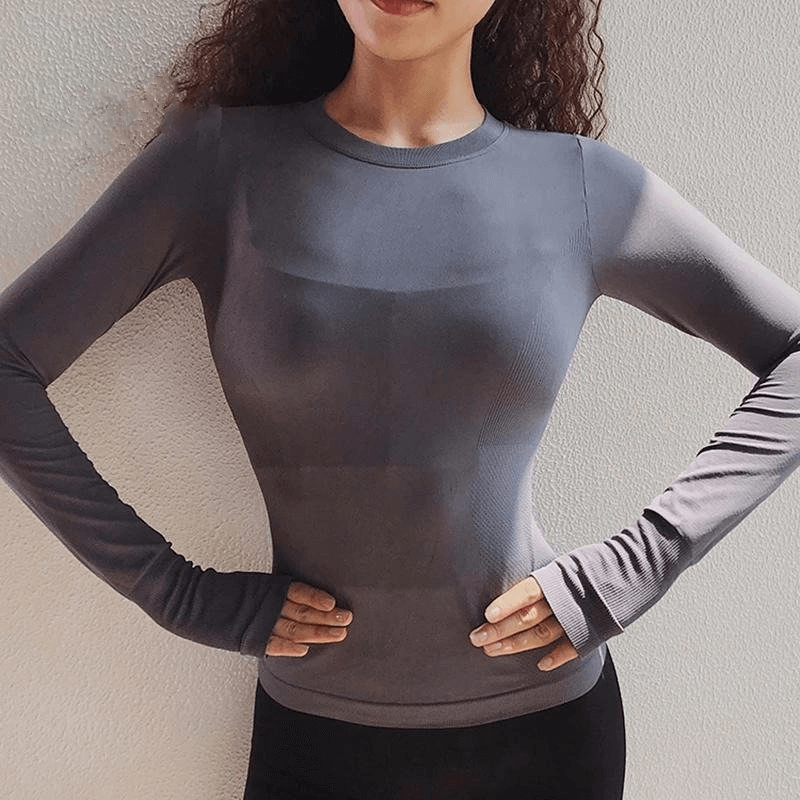 Woman wearing a slim fit gray long sleeve sports top with thumb holes, ideal for workouts; breathable spandex fabric emphasizes comfort.